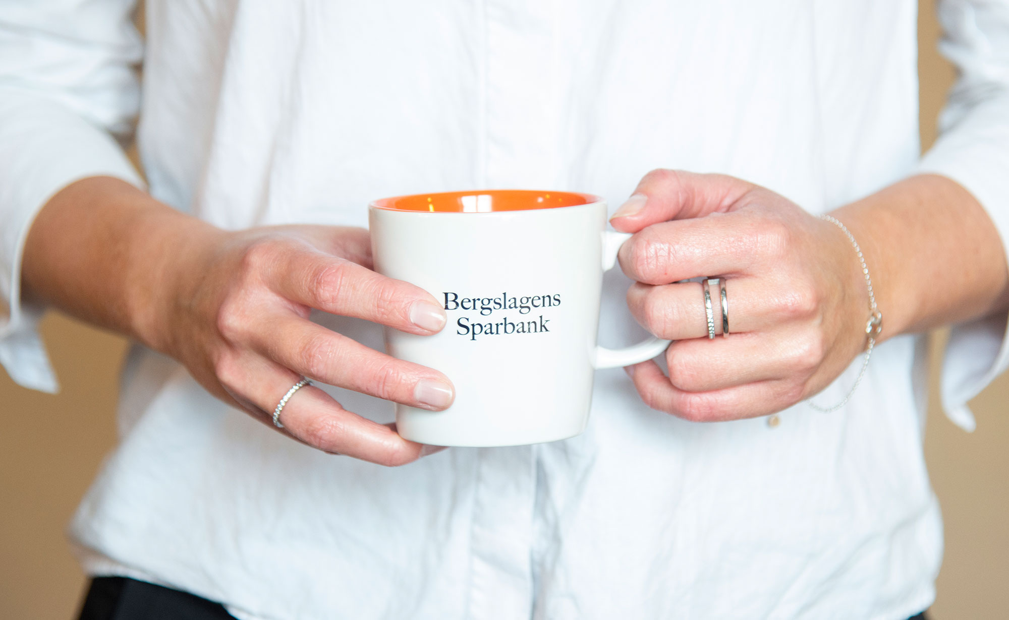 Woman holding a cup of coffee with Bergslagens Sparbank printed on the side